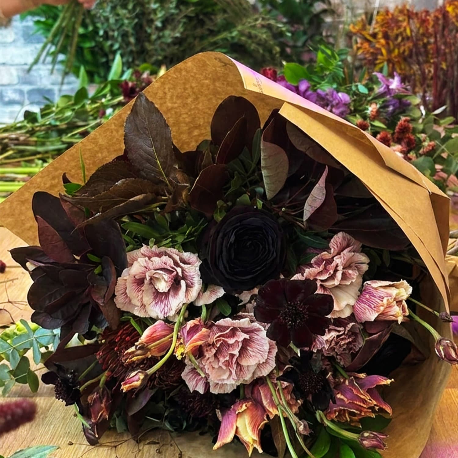 Ramo floral de otoño estilo Dark Romance empaquetado con floristería en tonos burdeos, rosa y negro.