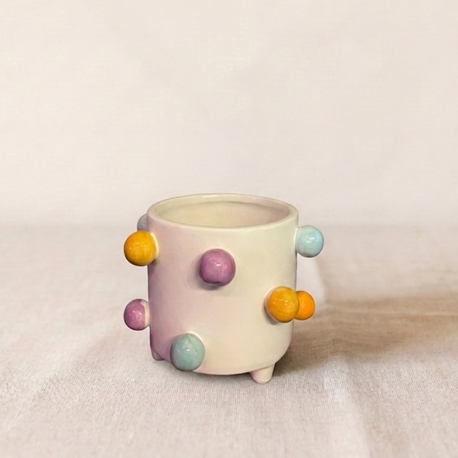 Maceta de cerámica blanca Color Dots con relieves esféricos de colores pastel amarillos, lilas y celestes sobre fondo claro.