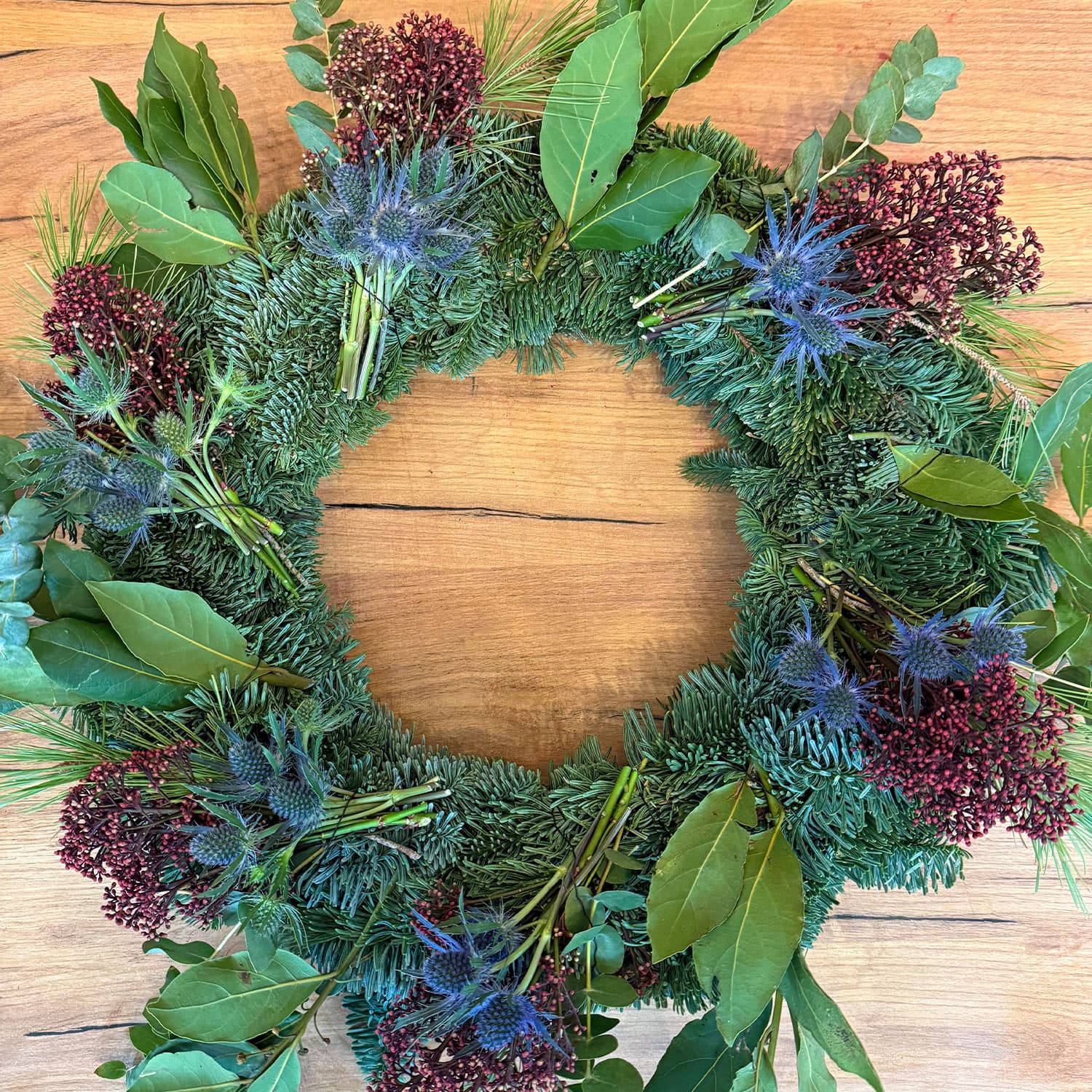 Corona de Navidad natural hecha a mano con pino fresco, eucalipto y piñas sobre fondo madera